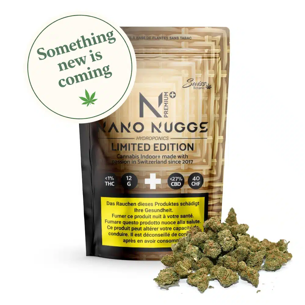 Un paquet de Fleurs de CBD indoor Nano Nuggs Premium Limited Edition - Gold 1% THC avec des bourgeons renversés devant, affichant une étiquette circulaire qui dit "Something new is coming" et comporte une icône de feuille de cannabis.